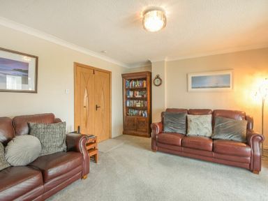 A living room with two brown leather sofas cushions a wooden bookshelf and a floor lamp at Creel Cottage Amble