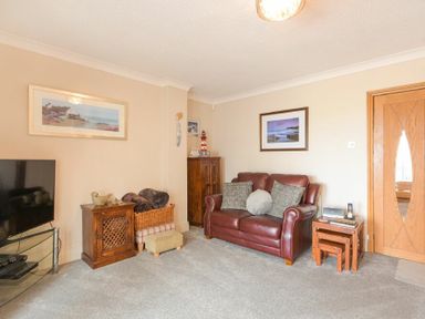 A living room with a leather sofa two framed pictures small wooden cabinets and a television at Creel Cottage Amble