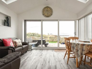 A living room with leather sofas and a dining table next to large sliding glass doors at Creel Cottage Amble