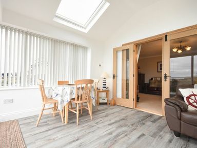 A dining area with a table and chairs next to large vertical blinds and a skylight at Creel Cottage Amble