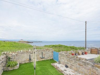 An outdoor area with stone walls a blue gate grass and sea view at Creel Cottage Amble