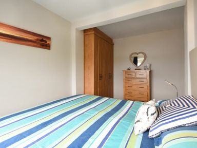 A bedroom with a bed with striped bedding a wooden wardrobe a wooden chest of drawers and a heart shaped mirror at Creel Cottage Amble