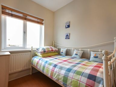 A small bedroom with a single metal frame bed with multicolored checkered bedding and three boat motif pillows at Creel Cottage Amble