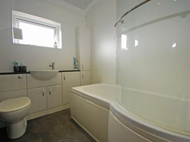 A bathroom with a bathtub a toilet a sink and cabinets at Creel Cottage Amble