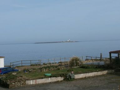 A coastal view with a garden area a fence and a lighthouse on an island in the distance at Creel Cottage Amble