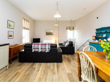 A living room with black sofas wooden dining table with chairs and blue cabinet at Baysyde in Alnmouth