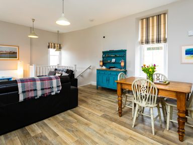 A living room with black leather sofas a wooden dining table with chairs a blue cabinet and flowers on the table at Baysyde in Alnmouth