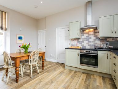 A kitchen with a wooden dining table and chairs and built in cabinets and oven at Baysyde in Alnmouth