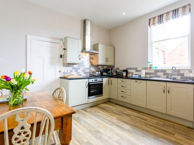 A kitchen with cabinets a stove a wooden dining table with flowers and chairs at Baysyde in Alnmouth
