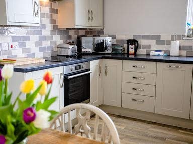 A kitchen with white cabinets black countertops a microwave oven toaster kettle and flowers on a table at Baysyde in Alnmouth