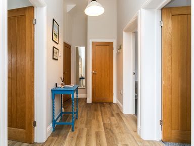 A hallway with wooden doors a blue table a wall mirror and two framed pictures at Baysyde in Alnmouth