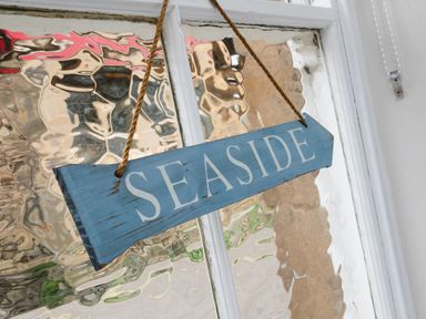 A blue wooden sign with the word seaside hanging on a textured glass door at Baysyde in Alnmouth