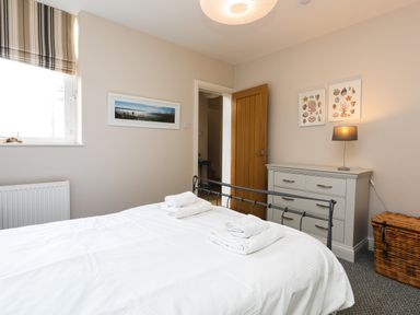A bedroom with a bed, chest of drawers, lamp, wicker basket, and framed pictures at Baysyde in Alnmouth