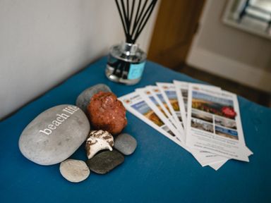 A collection of stones including one engraved with beach life a reed diffuser and several brochures on a blue surface at Baysyde in Alnmouth