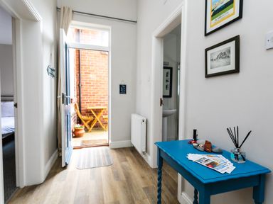 A hallway with a blue table and brochures near an open door leading to a small outdoor seating area at Baysyde in Alnmouth