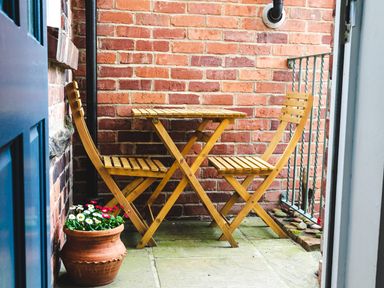 A small outdoor seating area with a wooden table and two wooden chairs next to a brick wall and a flower pot at Baysyde in Alnmouth