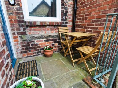 A small outdoor patio with wooden table and chairs pots with flowers and brick walls at Baysyde in Alnmouth