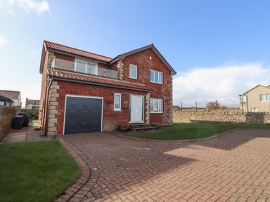 A two-story brick house with a garage and a driveway surrounded by grass and stone walls at Rathowen in Beadnell