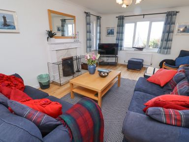 A living room with a wooden coffee table between two blue sofas and a television near the windows at Rathowen in Beadnell