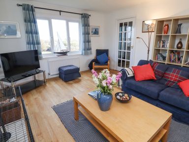 A living room with a blue sofa red cushions coffee table flowers books and a television at Rathowen in Beadnell