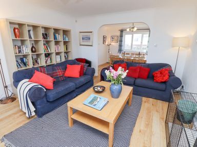 A living room with blue sofas and red cushions a wooden coffee table and a bookshelf at Rathowen in Beadnell