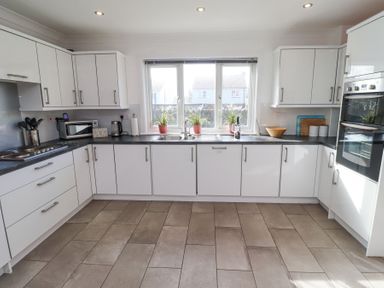 A kitchen with white cabinets plants on the windowsill a microwave oven and a double oven at Rathowen in Beadnell