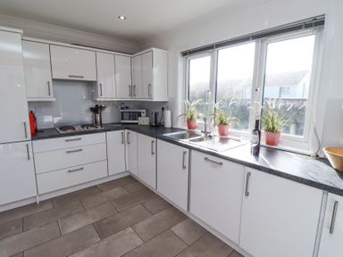 A kitchen with white cabinets a countertop with a sink and three plants on the windowsill at Rathowen Beadnell