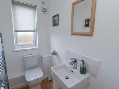 A bathroom with a toilet sink mirror and window at Rathowen in Beadnell