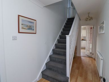 A hallway with wooden floor a grey carpeted staircase and a door leading to a kitchen at Rathowen in Beadnell