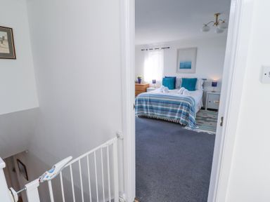 A bedroom with a bed covered in blue and white bedding viewed through a doorway at Rathowen in Beadnell