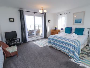 A bedroom with a double bed, television on a stand, chair, dresser, rugs, and sliding glass doors leading to a balcony at Rathowen in Beadnell