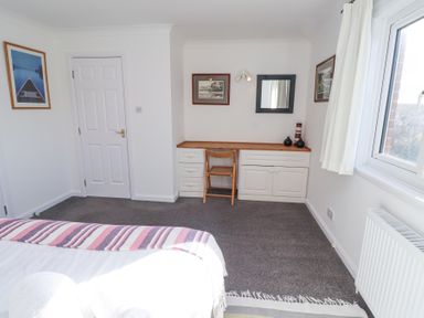A bedroom with a bed, built-in desk with chair, framed pictures, a window, and a radiator at Rathowen Beadnell