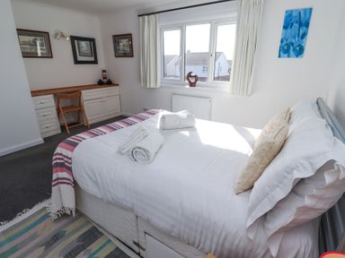 A bedroom with a made bed folded towels a desk with a chair and framed pictures on the wall at Rathowen in Beadnell
