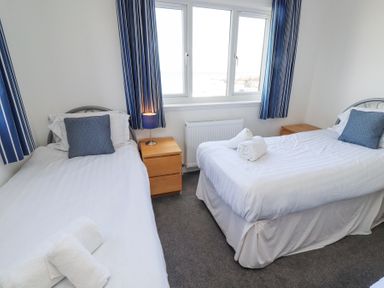 A bedroom with two single beds with blue pillows and towels on beds a nightstand with a lamp between beds and a window with blue curtains at Rathowen in Beadnell