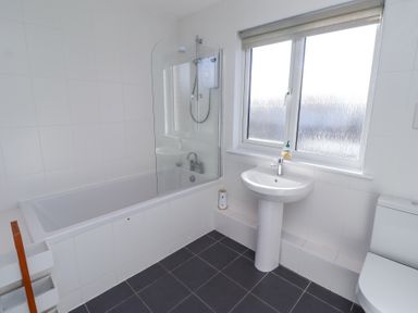 A bathroom with a bathtub shower combination a pedestal sink a toilet and a window at Rathowen in Beadnell