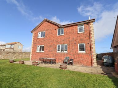 A brick house with several windows and a patio with table and chairs in a grassy yard at Rathowen in Beadnell