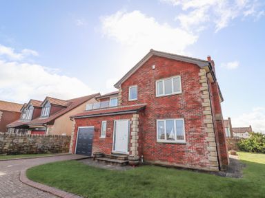 A brick detached house with driveway garage and grass lawn at Rathowen in Beadnell