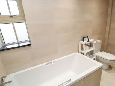A bathroom with a bathtub toilet window and a small white shelving unit at Nook Cottage in Embleton