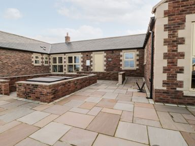 A paved courtyard with brick walls and windows at Nook Cottage in Embleton