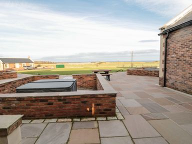 An outdoor patio area with brick walls a covered hot tub a picnic table and grassy fields in the background at Nook Cottage in Embleton