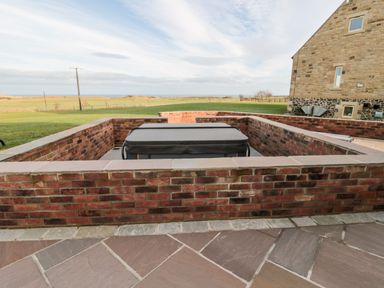 A covered hot tub set in a recessed brick patio with a stone floor and a grassy field in the background at Nook Cottage in Embleton