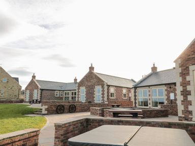 An outdoor courtyard area with brick buildings and picnic tables at Nook Cottage in Embleton