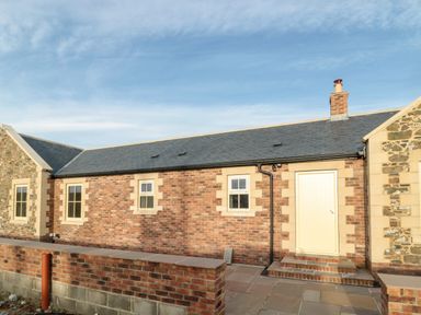 A brick house exterior with three small windows a door and a chimney at Nook Cottage in Embleton