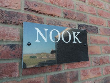 A black rectangular sign with the word NOOK on a red brick wall at Nook Cottage in Embleton