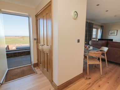 An entryway with wooden double doors and a doormat next to a dining area with a table, chairs, and brown sofas at Nook Cottage in Embleton