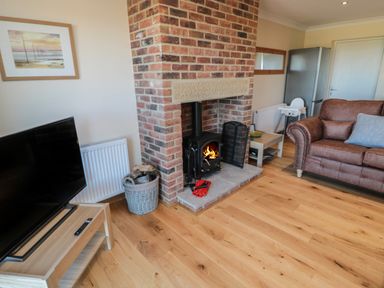 A living room with a brick fireplace wood stove brown sofa and a television at Nook Cottage in Embleton