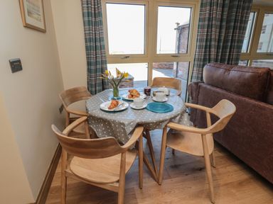 A dining area with a round table covered by a polka dot tablecloth and four wooden chairs at Nook Cottage in Embleton