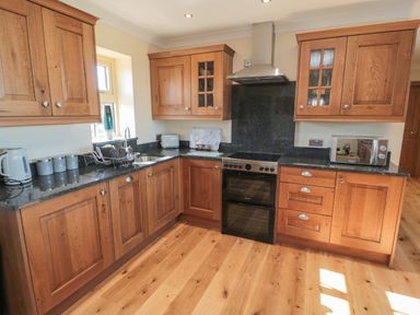 A kitchen with wooden cabinets black countertops a stove microwave kettle and a sink at Nook Cottage in Embleton