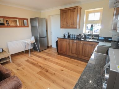 A kitchen with wooden cabinets a refrigerator a sink high chair and countertop appliances at Nook Cottage in Embleton