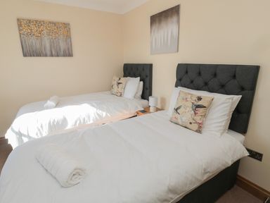 A bedroom with two single beds with tufted headboards and floral cushions at Nook Cottage in Embleton
